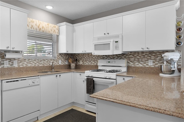 kitchen with decorative backsplash, white appliances, a textured ceiling, and a sink