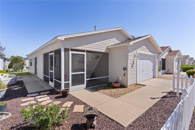 view of property exterior featuring fence, a residential view, concrete driveway, an attached garage, and a sunroom