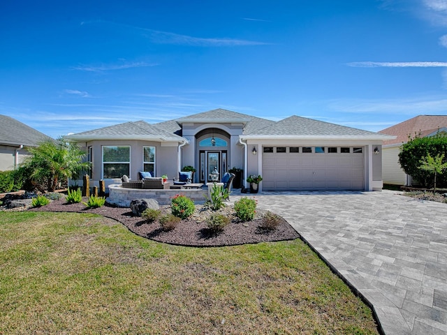 view of front of property featuring stucco siding, decorative driveway, a front yard, an attached garage, and an outdoor hangout area