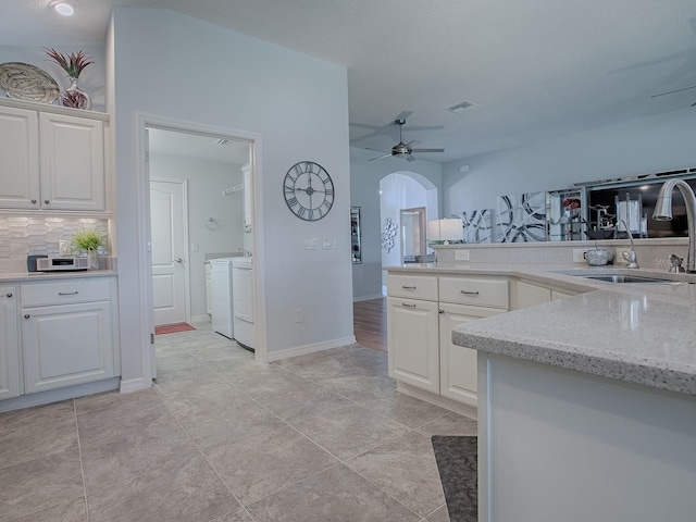 kitchen with visible vents, ceiling fan, washer and clothes dryer, white cabinetry, and a sink