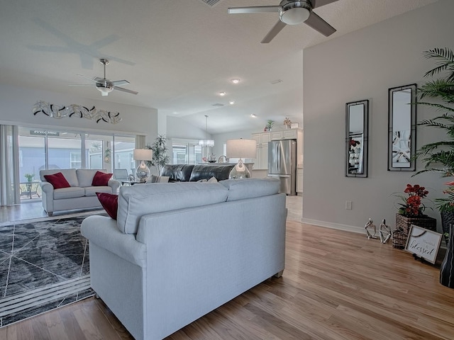 living room featuring vaulted ceiling, ceiling fan with notable chandelier, and light wood-type flooring