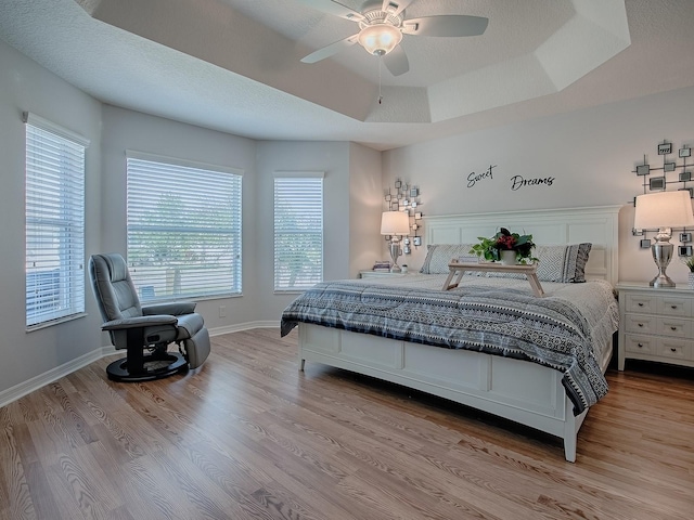 bedroom featuring a tray ceiling, baseboards, a textured ceiling, and light wood-style flooring