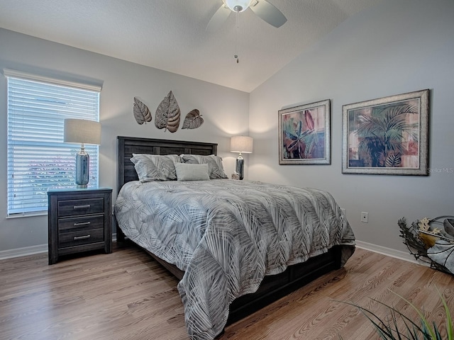 bedroom with baseboards, vaulted ceiling, light wood-style floors, a textured ceiling, and a ceiling fan