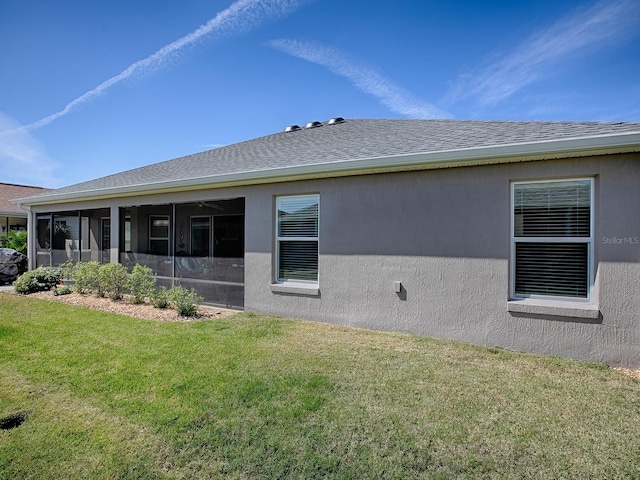 rear view of house with a yard, a shingled roof, stucco siding, and a sunroom