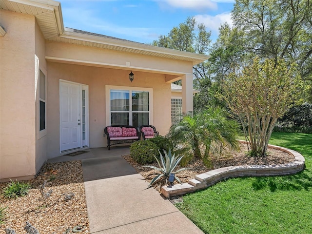 view of exterior entry featuring a yard, a porch, and stucco siding