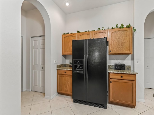 kitchen with baseboards, light stone counters, light tile patterned flooring, black refrigerator with ice dispenser, and arched walkways