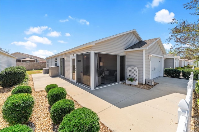 rear view of house featuring fence, concrete driveway, cooling unit, a sunroom, and an attached garage