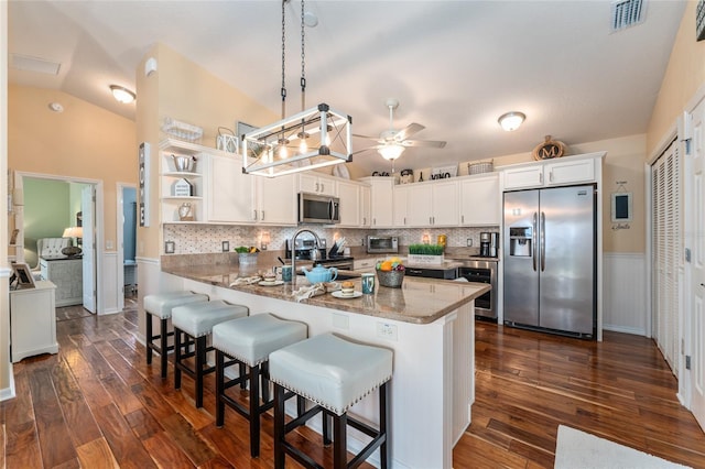 kitchen with visible vents, a peninsula, stainless steel appliances, white cabinetry, and a sink