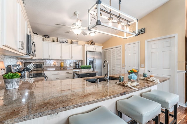 kitchen featuring decorative backsplash, appliances with stainless steel finishes, a peninsula, white cabinetry, and a ceiling fan