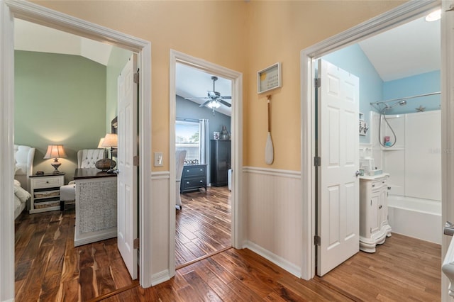 hallway featuring wainscoting, wood finished floors, and vaulted ceiling