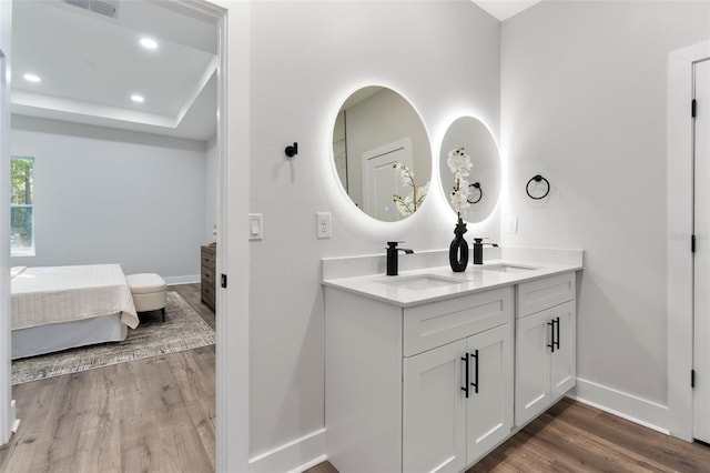 ensuite bathroom featuring double vanity, wood finished floors, baseboards, and a sink