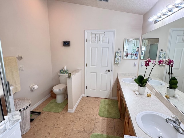 bathroom featuring double vanity, a sink, tile patterned flooring, a textured ceiling, and toilet