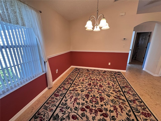 unfurnished dining area featuring baseboards, lofted ceiling, an inviting chandelier, arched walkways, and a textured ceiling