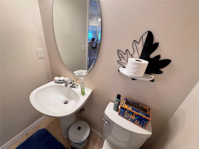 half bath with tile patterned floors, toilet, baseboards, and a sink