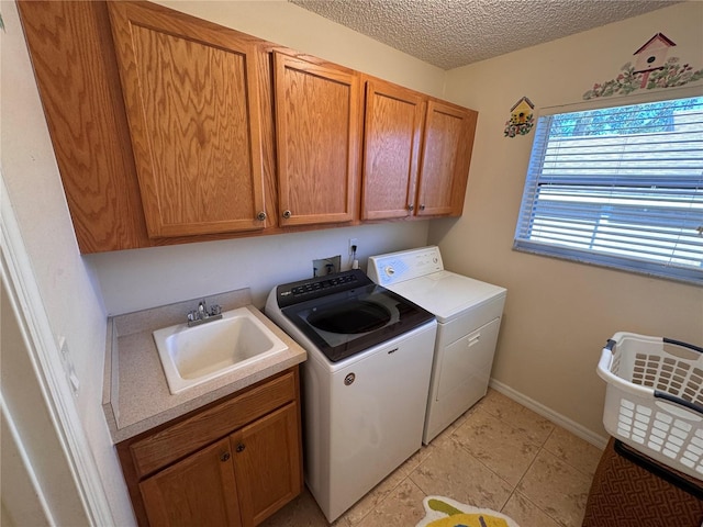 laundry area with baseboards, cabinet space, a textured ceiling, independent washer and dryer, and a sink