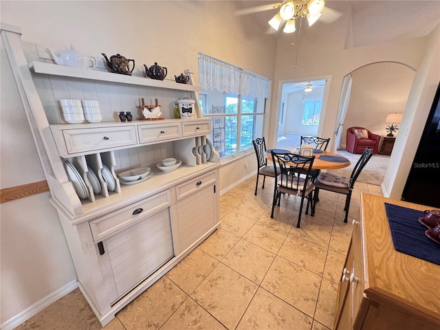 dining room featuring light tile patterned floors, arched walkways, baseboards, and ceiling fan