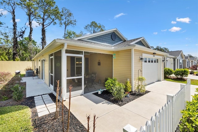 view of property exterior with driveway, fence private yard, a garage, and a sunroom