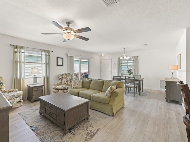 living area with light wood-type flooring, visible vents, and ceiling fan with notable chandelier