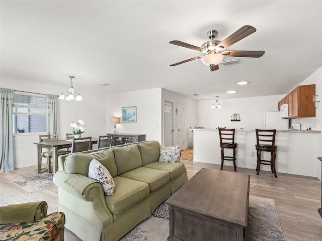 living room featuring light wood-style flooring, ceiling fan with notable chandelier, and visible vents