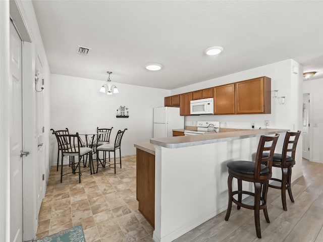 kitchen featuring visible vents, a kitchen breakfast bar, a peninsula, brown cabinetry, and white appliances