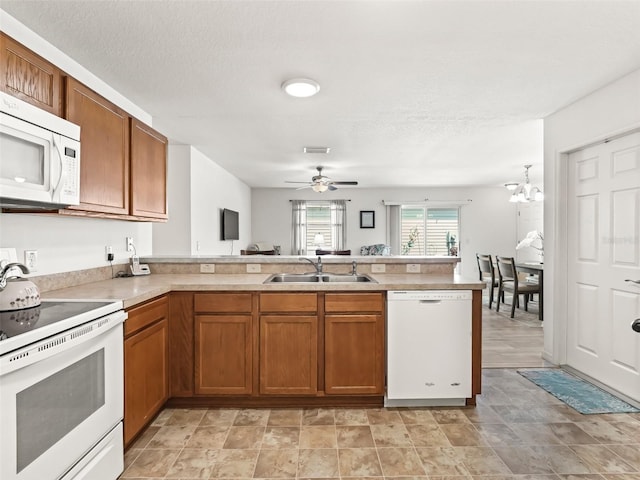 kitchen featuring white appliances, brown cabinetry, a peninsula, a sink, and light countertops