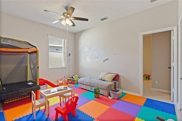 recreation room featuring baseboards, visible vents, a textured ceiling, and a ceiling fan