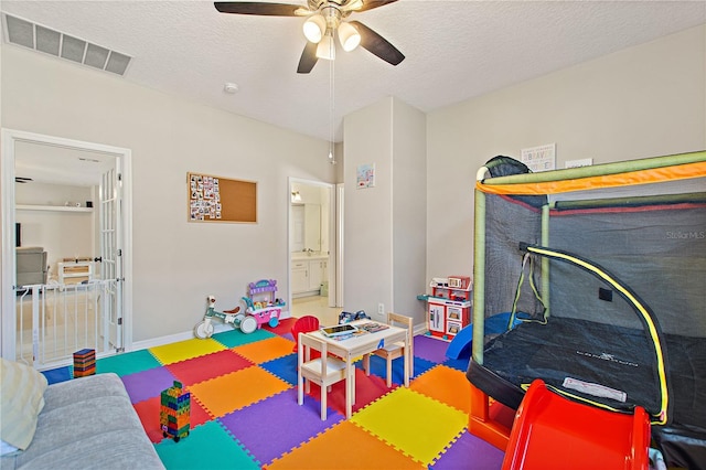 recreation room featuring visible vents, ceiling fan, a textured ceiling, and baseboards