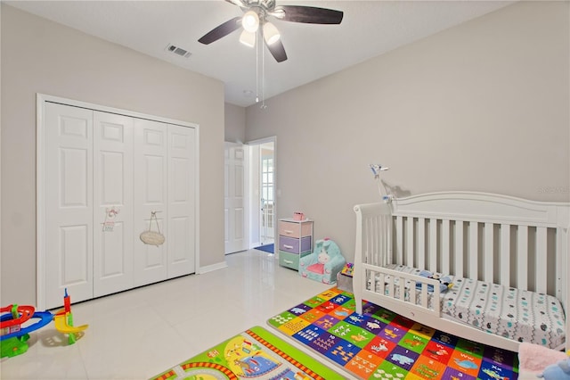 bedroom with visible vents, ceiling fan, tile patterned flooring, a crib, and a closet