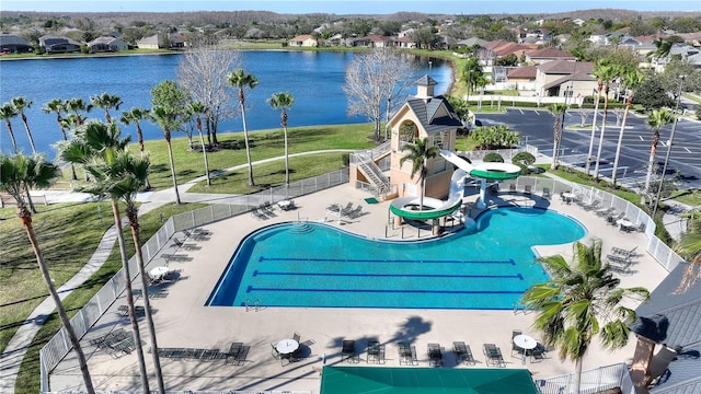 pool with a patio area, fence, a water view, and a water slide