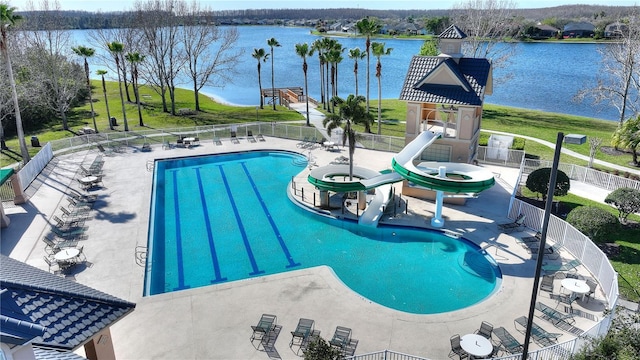 community pool with a patio, fence, a water view, and a water slide