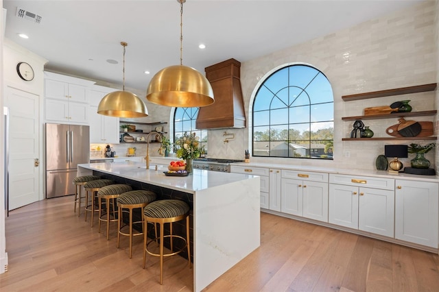 kitchen featuring visible vents, open shelves, light countertops, custom range hood, and stainless steel fridge