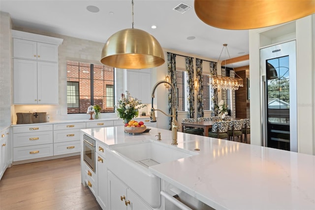 kitchen featuring visible vents, a sink, pendant lighting, white cabinetry, and stainless steel microwave