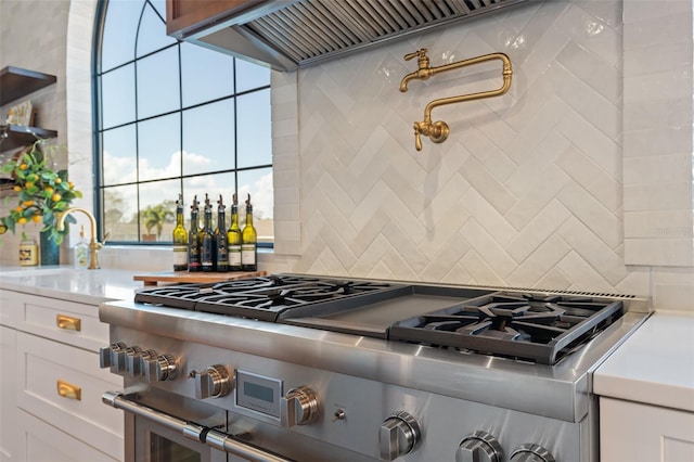 kitchen with backsplash, light countertops, stainless steel stove, custom exhaust hood, and white cabinetry