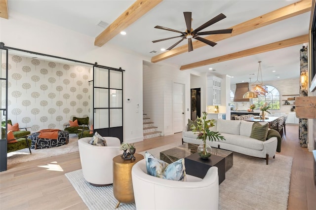 living area featuring wood finished floors, visible vents, stairs, a barn door, and beamed ceiling