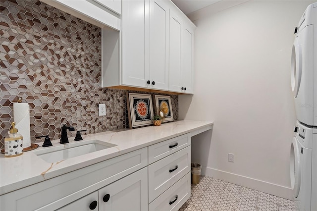 kitchen with baseboards, a sink, decorative backsplash, stacked washer and dryer, and white cabinets