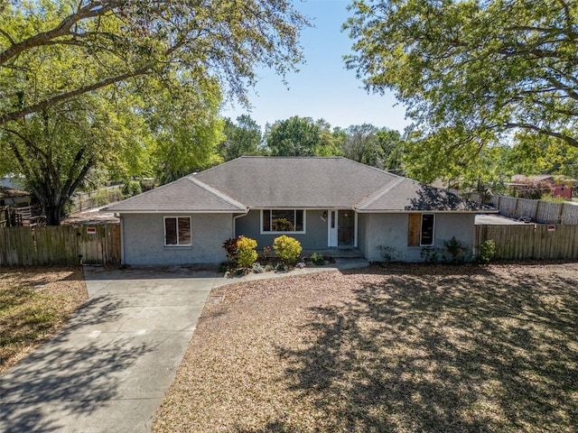 ranch-style home featuring driveway, a shingled roof, and fence