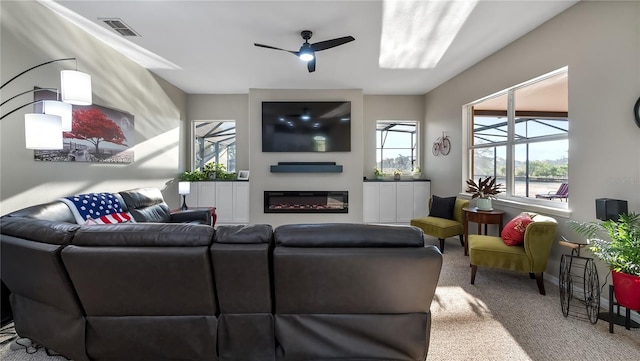 carpeted living area with visible vents, a ceiling fan, and a glass covered fireplace