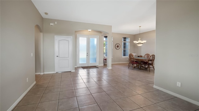 foyer featuring baseboards, french doors, arched walkways, and a chandelier