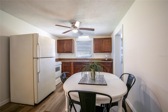 kitchen with brown cabinets, white appliances, dark wood-type flooring, and a ceiling fan