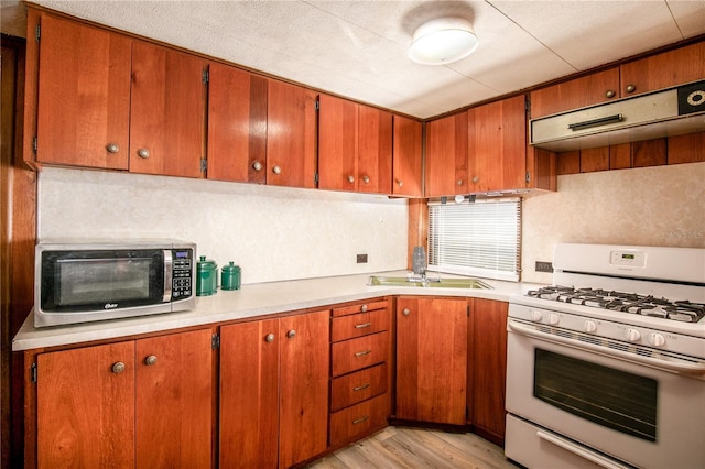 kitchen featuring white gas stove, a sink, light countertops, stainless steel microwave, and light wood-type flooring