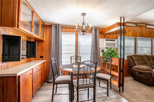 dining space featuring light wood-style floors, wooden walls, a chandelier, and a textured ceiling