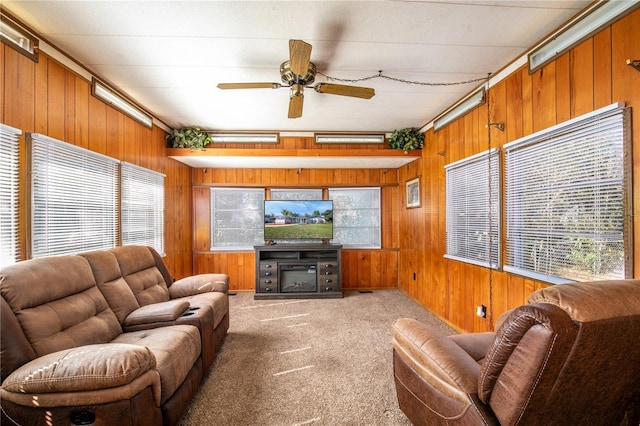 carpeted living area with a glass covered fireplace, wooden walls, and ceiling fan