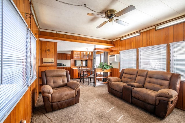 carpeted living room featuring wooden walls, an AC wall unit, and ceiling fan with notable chandelier