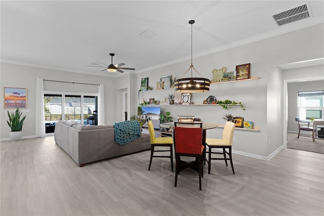 dining space featuring baseboards, visible vents, light wood-style flooring, ceiling fan, and ornamental molding