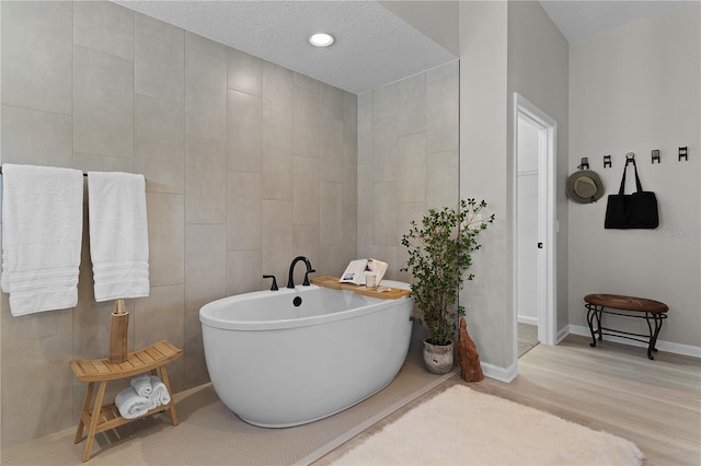 bathroom featuring wood finished floors, baseboards, a freestanding bath, a textured ceiling, and tile walls