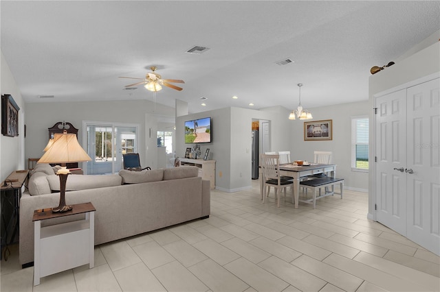 living area with a wealth of natural light, visible vents, ceiling fan with notable chandelier, and vaulted ceiling