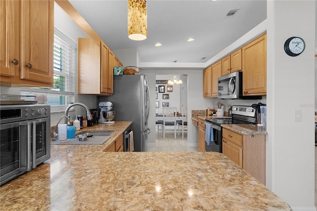 kitchen featuring visible vents, light stone countertops, appliances with stainless steel finishes, an inviting chandelier, and a sink