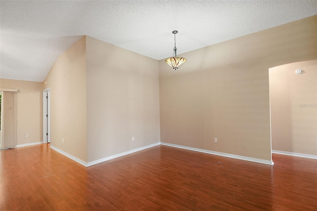 empty room with baseboards, wood finished floors, arched walkways, and a textured ceiling