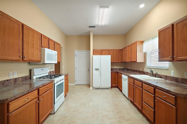 kitchen featuring dark countertops, visible vents, brown cabinets, white appliances, and a sink