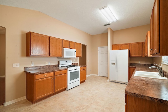 kitchen featuring white appliances, brown cabinetry, dark countertops, and a sink